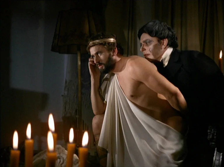 Satan’s Brew (1976) movie still: medium — A dimly lit room with candles in the foreground creating a warm, flickering light. A man in a toga sits…