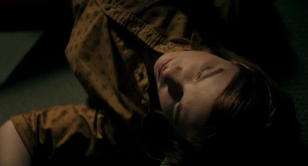 Ouija: Origin of Evil (2016) movie still: closeup — A person lies on a dark, carpeted floor in a dimly lit room. The young woman rests with her eyes…