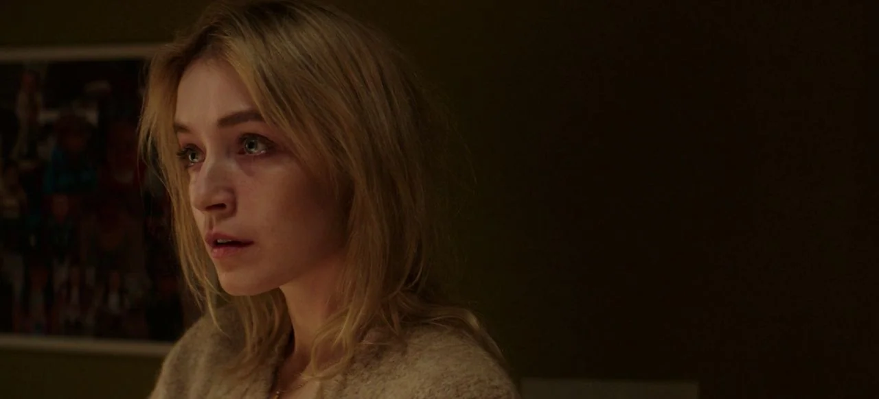 A Good Woman Is Hard To Find (2019) movie still: closeup — A dimly lit room features a woman centered against a dark wall. She looks toward the left…