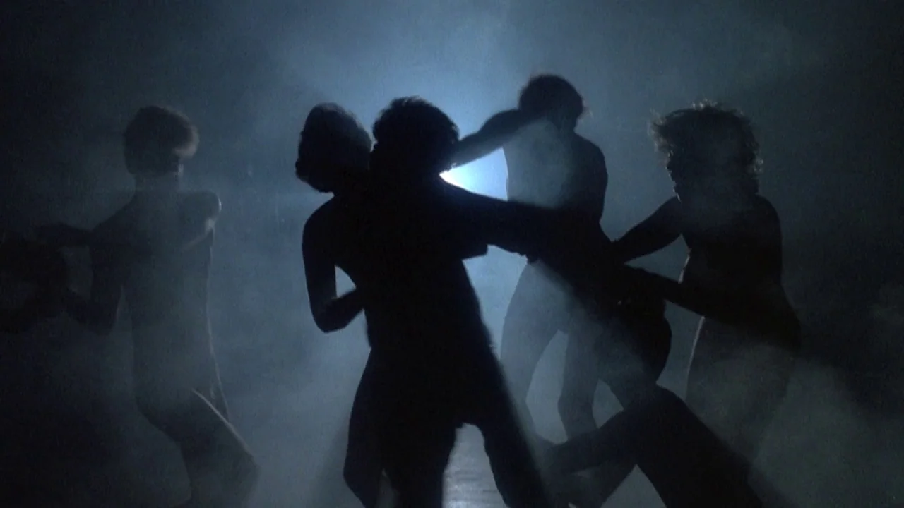 Re-Animator (1985) movie still: medium — A group of people dance in a dark room filled with thick swirling smoke. Bright backlighting creates…