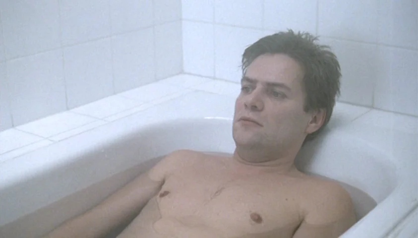 The Seventh Continent (1989) movie still: medium — A man sits in a white-tiled bathtub filled with murky water. He looks ahead with a blank…