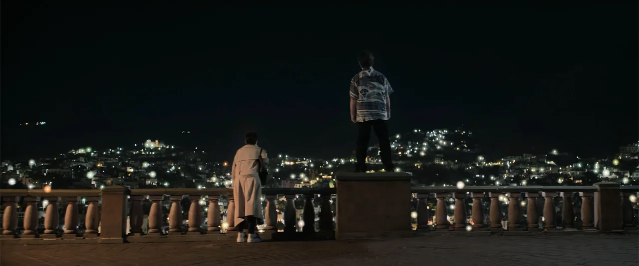 Angel Flight THE MOVIE (2026) movie still: wide — A stone terrace with decorative balustrades overlooks a vast, illuminated city at night. Two men…