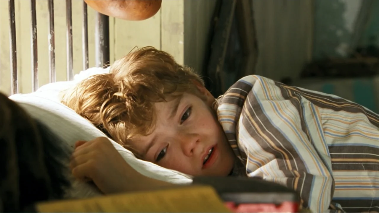 Nanny McPhee and the Big Bang (2010) movie still: closeup — A child rests in a bed with a wooden headboard in a simple room. The young boy looks…