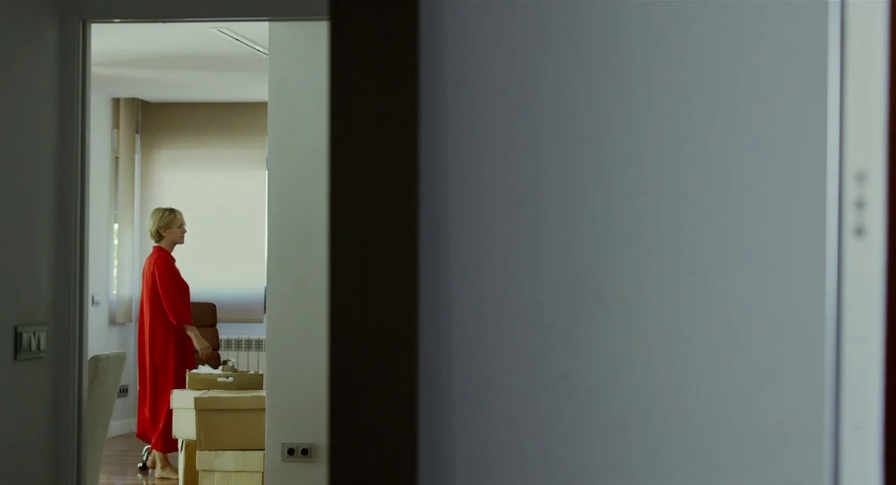 Julieta (2016) movie still: wide — A spare interior space featuring cardboard boxes stacked on the wooden floor. A woman in a red dress stands…