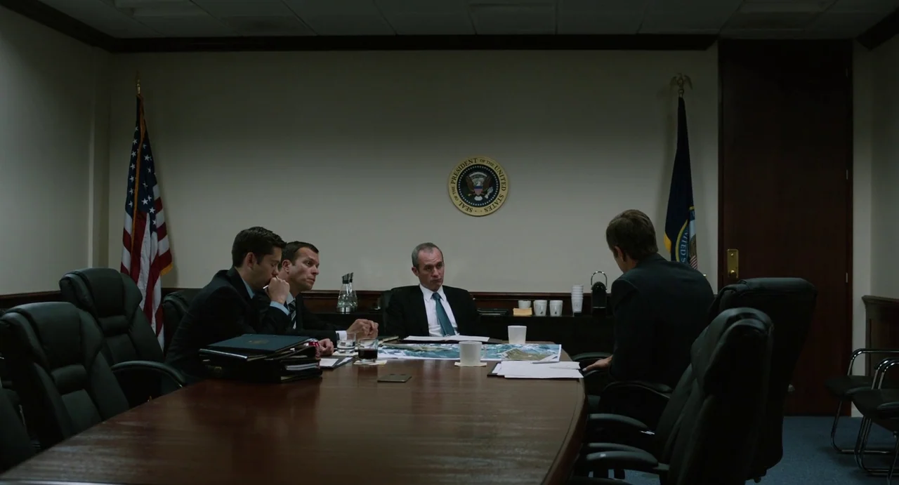 Zero Dark Thirty (2012) movie still: wide — A austere government conference room features plain walls with an official presidential seal emblem.…