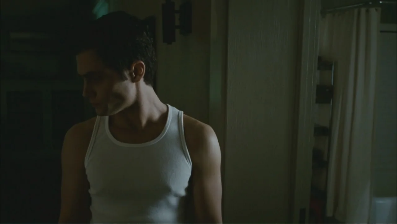 The Stepfather (2009) movie still: medium — A dimly lit room features a doorway leading into a tiled bathroom space. A young man in a white tank top…