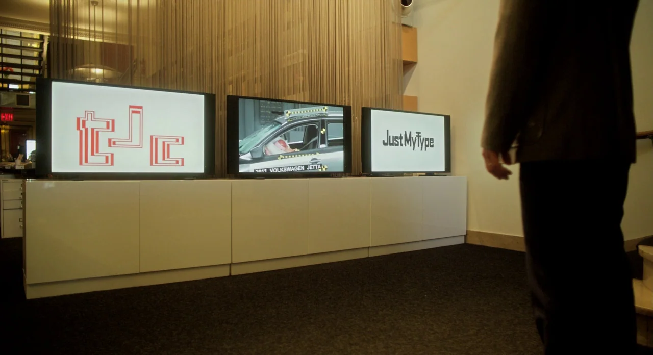 Side Effects (2013) movie still: medium — A dark gallery space features three television monitors mounted on a low white cabinet. A person in a dark…