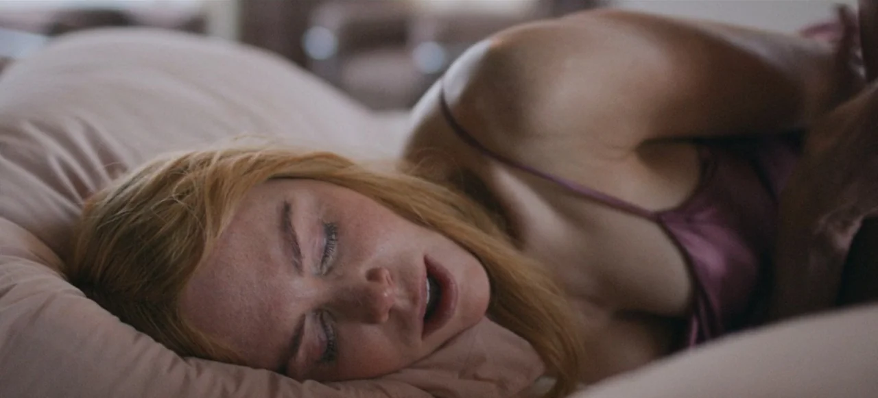 Babygirl (2024) movie still: closeup — A person rests in a bed with soft pink pillows. The subject lies on their side with eyes closed.