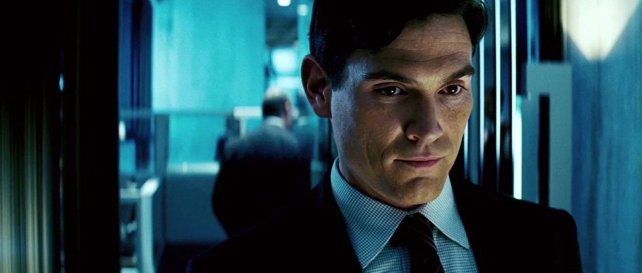 Down With Love (2003) movie still: closeup — A modern corridor interior with glass walls and cool blue illumination. A man in a dark suit stands in…