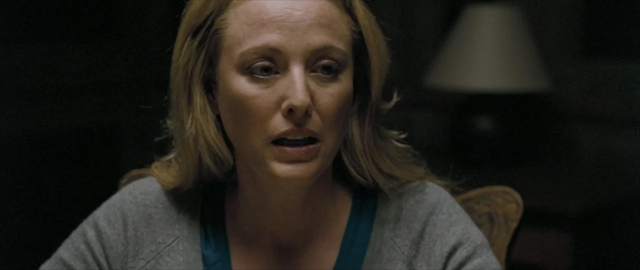 The Haunting in Connecticut (2009) movie still: closeup — A dimly lit interior room at night with a blurred lamp in the background. A woman in a…