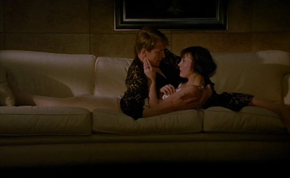 Mélo (1986) movie still: medium — A man and woman lie together on a white couch in a dimly lit room. They are positioned face to face with the man's…