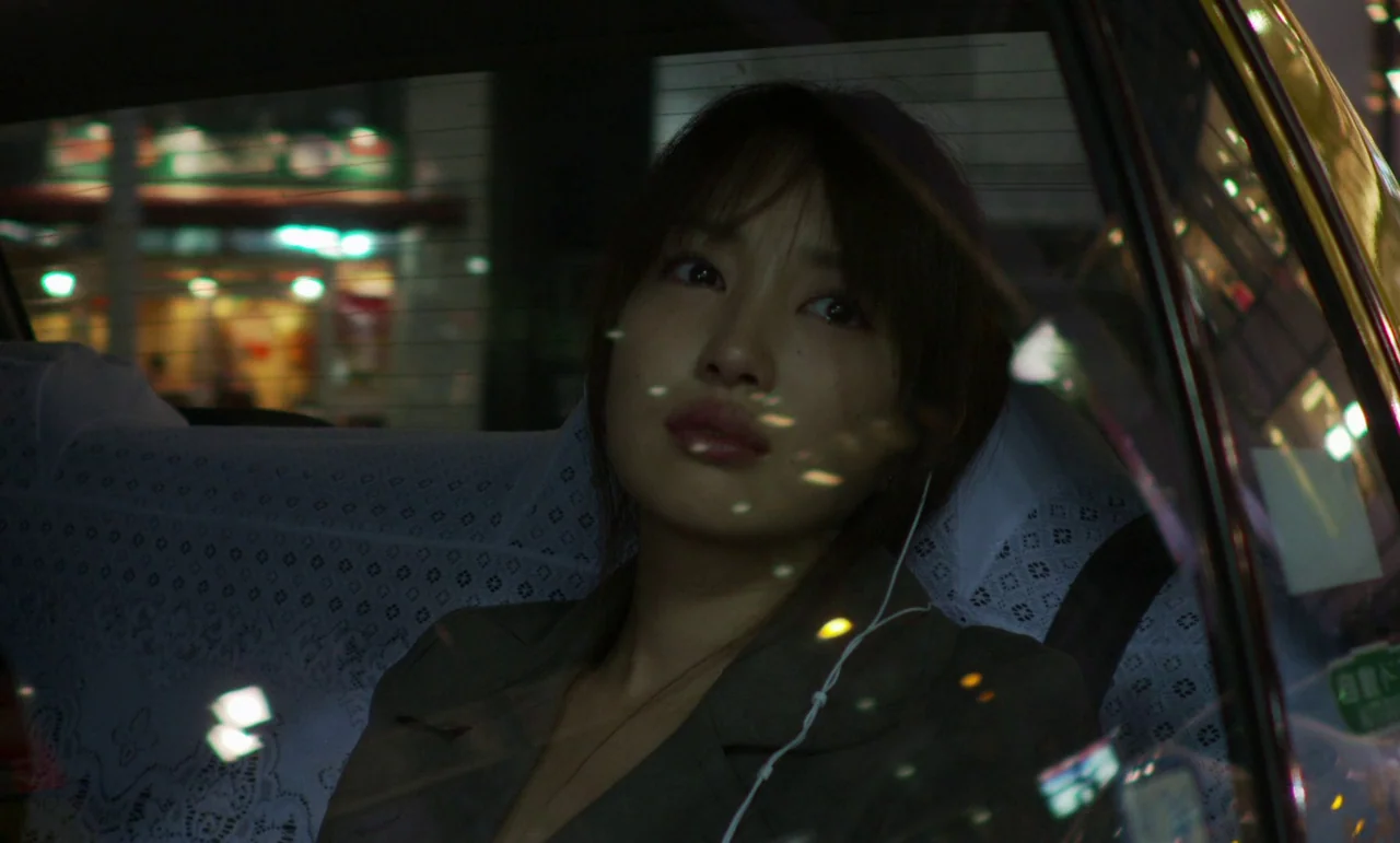 Like Someone In Love (2012) movie still: closeup — The interior of a taxi at night with white lace seat covers. A young woman sits in the back seat…