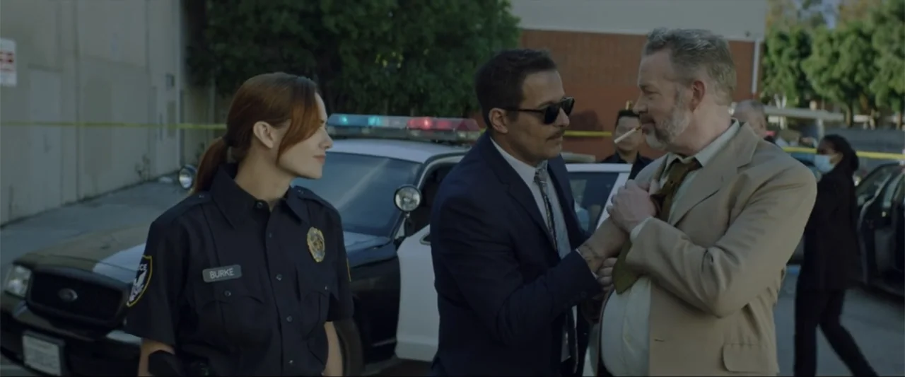 Gender Under Attack (2018) movie still: medium — An outdoor police investigation area featuring a parked squad car with yellow tape. A plainclothes…