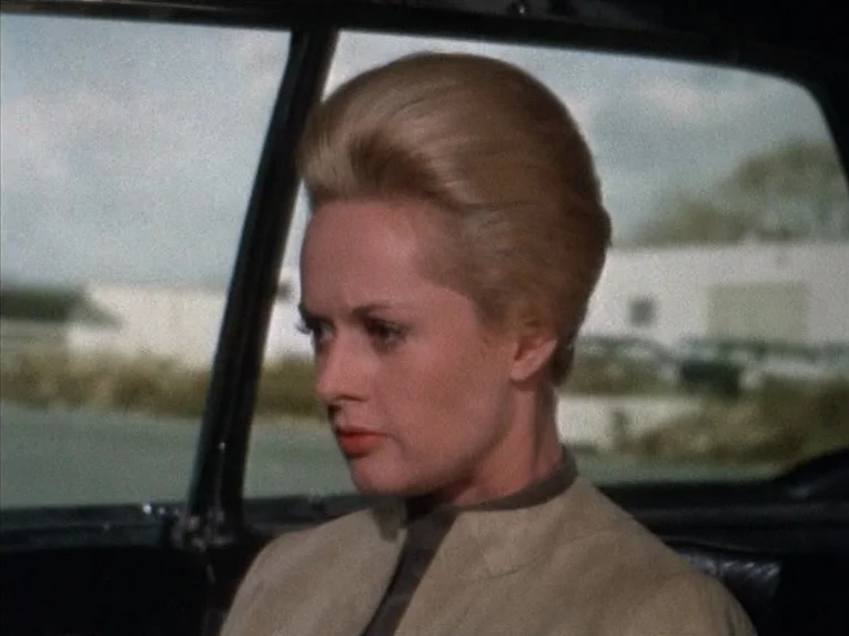 Marnie (1964) movie still: closeup — A woman sits inside a moving vehicle with a blurred exterior landscape visible behind. She looks forward while…