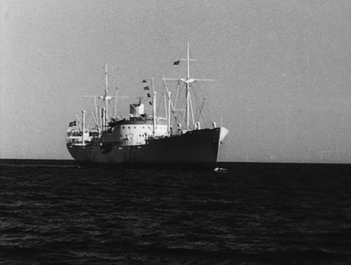 Port of Call (1948) movie still: wide — A cargo ship sails across a dark, rippled sea under a clear sky. The vessel is a multi-decked freighter with…
