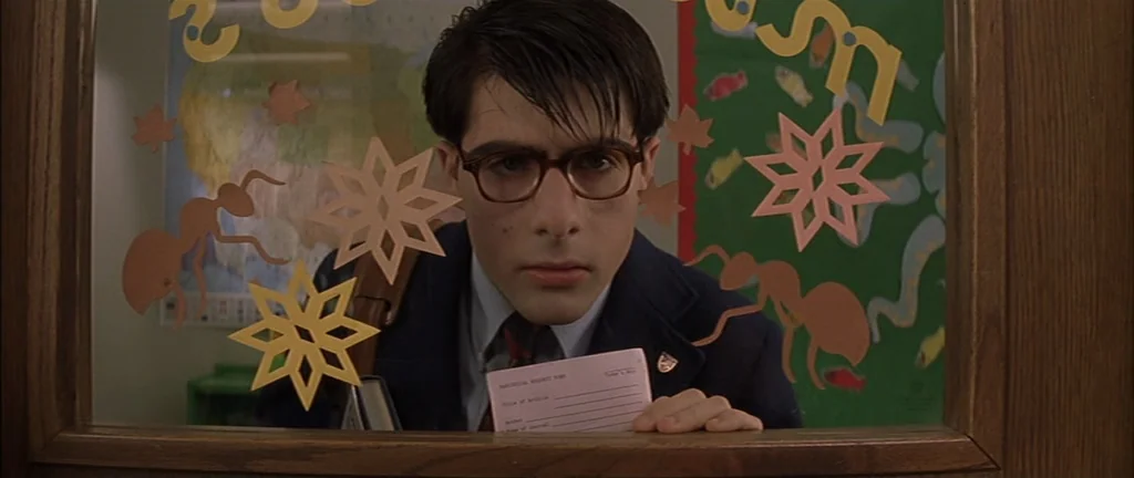 Rushmore (1998) movie still: closeup — A school library circulation desk features glass panels decorated with paper ants and stars. A young man…