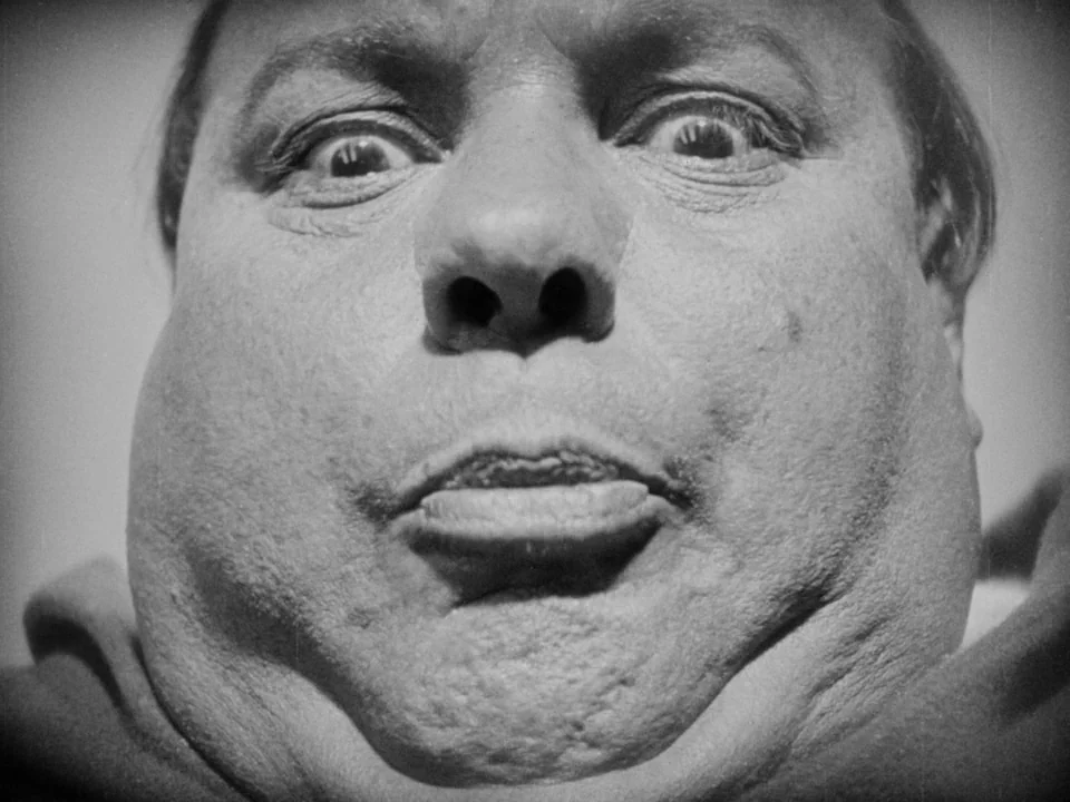 The Passion of Joan of Arc (1928) movie still: closeup — An extreme low-angle close-up captures a man's face against a plain, light background. The…