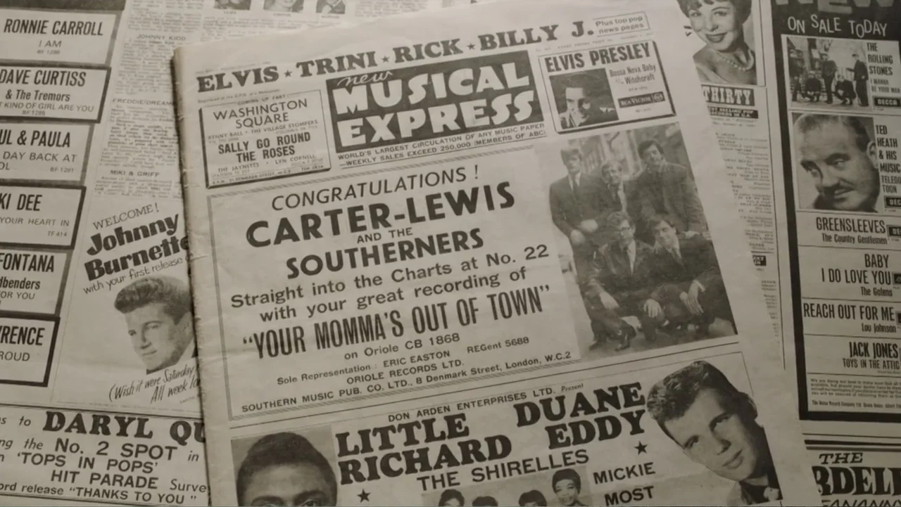 Becoming Led Zeppelin (2025) movie still: closeup — A close-up view shows a stack of 1960s music trade newspapers laid flat. Multiple headlines and…