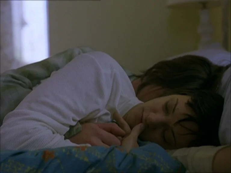 Last Days (2005) movie still: medium — A close view of a bed with blue patterned bedding and soft pillows. A man and woman sleep soundly together in…