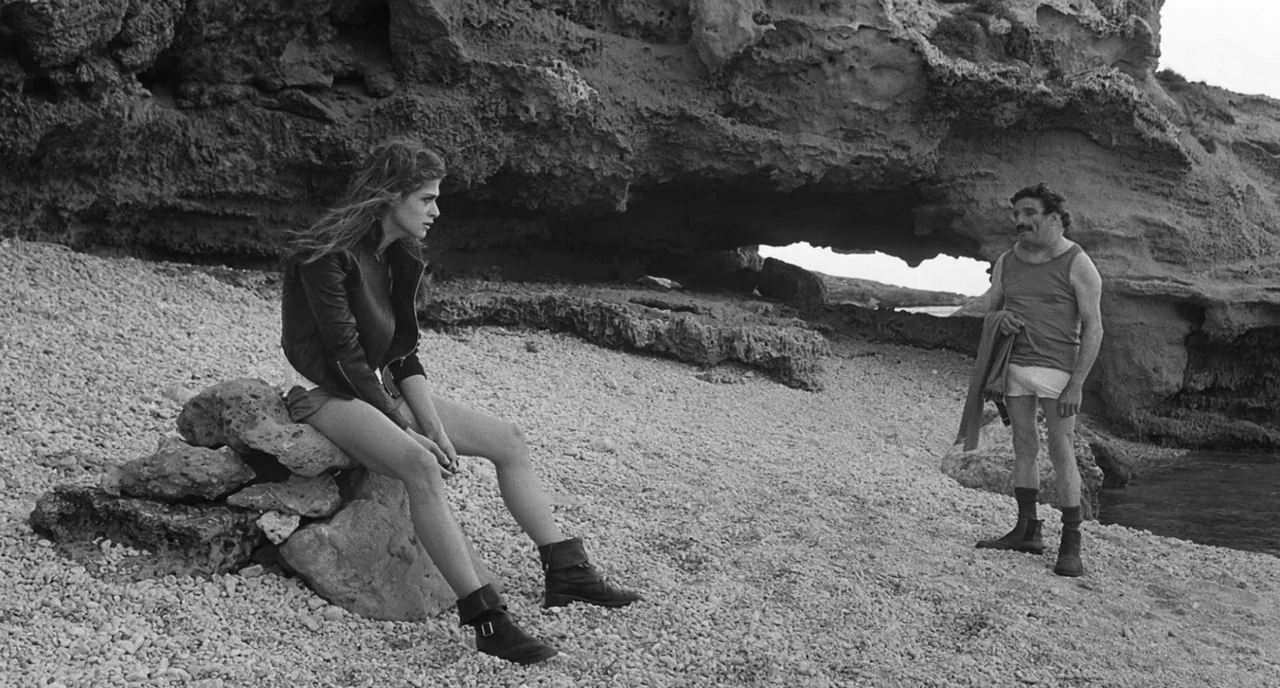 The Legend Of Kaspar Hauser (2012) movie still: fullbody — A rocky beach shoreline features a large weathered limestone formation with a natural…