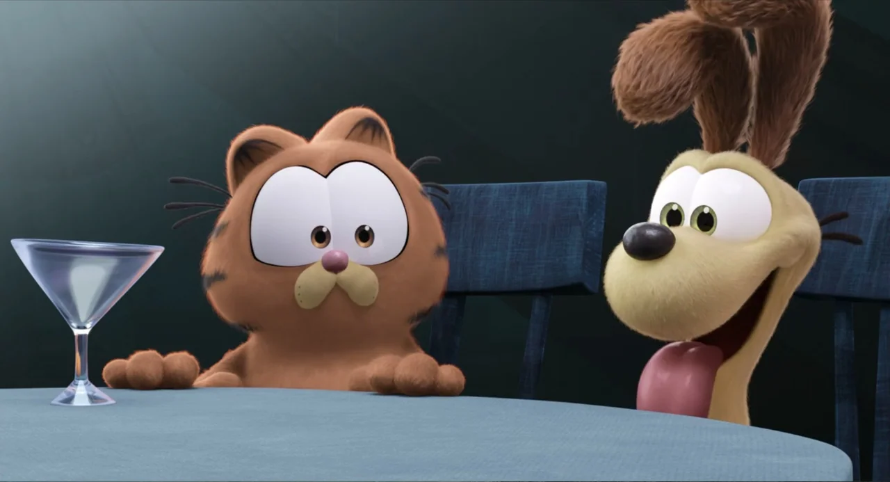 The Garfield Movie (2024) movie still: medium — An indoor setting features a table with a martini glass and blue chairs. A cartoon orange cat and a…