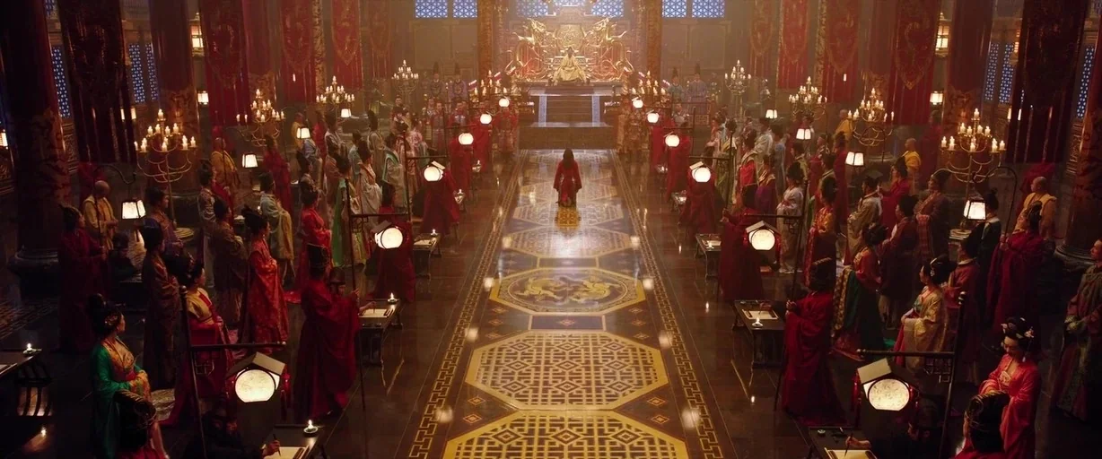 Mulan (2020) movie still: wide — A grand imperial hall features an ornate floor pattern and a distant raised throne. A single person kneels in the…