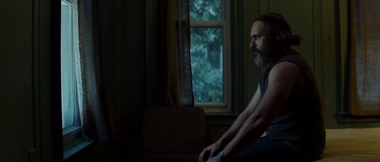You Were Never Really Here (2017) movie still: medium — A dimly lit room with muted green walls and two windows letting in light. A bearded man with…