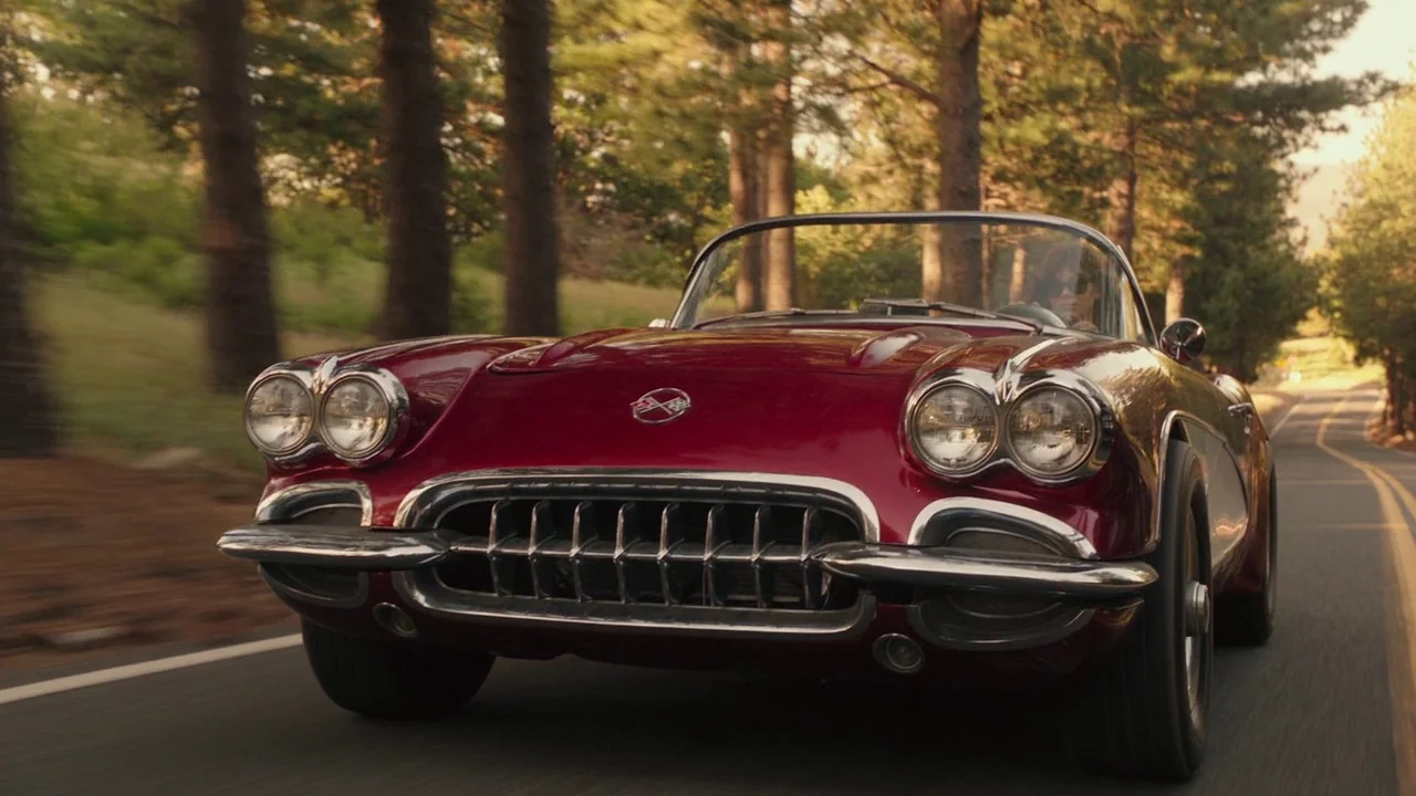 Bumblebee (2018) movie still: medium — A vintage red Corvette convertible drives along a winding road lined with tall trees. The setting is a rural…