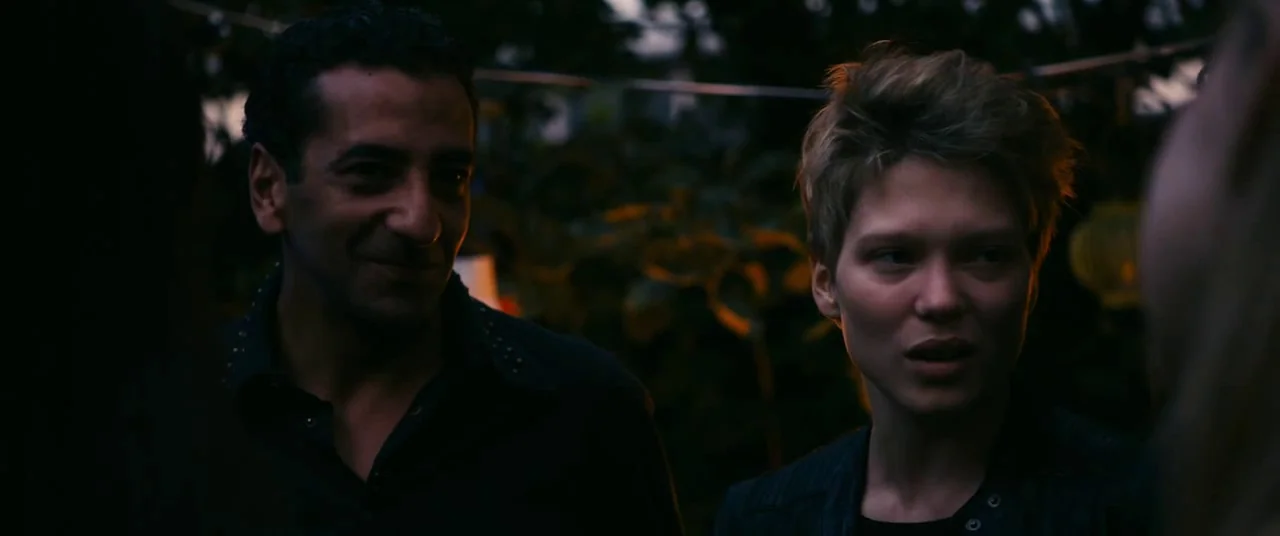 Blue Is The Warmest Colour (2013) movie still: medium — An outdoor evening setting with foliage visible in the out-of-focus background. A man and a…