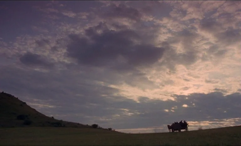 Yentl (1983) movie still: establishing — Rolling grassy hills extend under a cloudy sky during the late evening. A horse-drawn wagon carrying a…