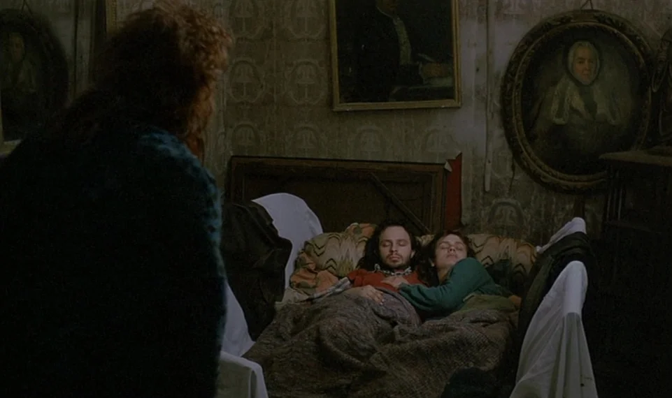Vagabond (1985) movie still: medium — A dimly lit room features patterned wallpaper and framed portraits hanging on the walls. A man and a woman…