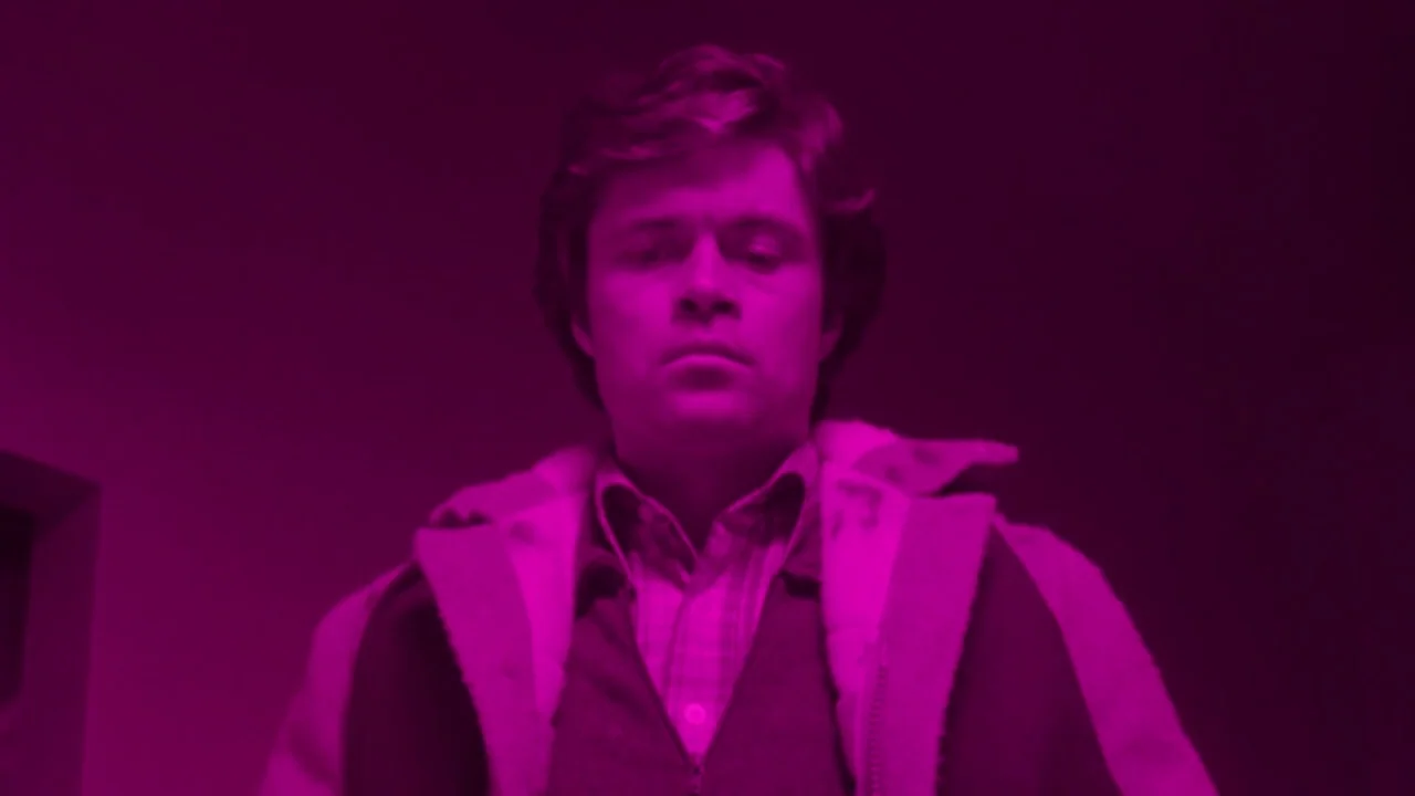 The Brood (1979) movie still: medium — An interior space is drenched in a saturated magenta light. A man looks directly toward the floor with a…