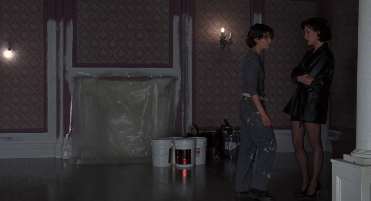 Bound (1996) movie still: fullbody — An interior room with patterned wallpaper features white paint patches around the trim. Two women stand on…