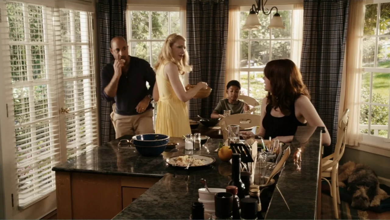 Easy A (2010) movie still: medium — A well-lit residential dining area features a large stone-topped island and plaid window curtains. Four people…