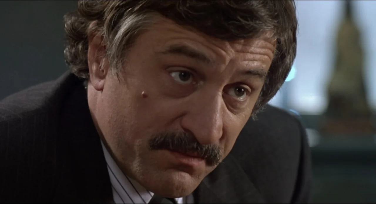 Cop Land (1997) movie still: closeup — An interior office space with blurred neutral background elements and soft light. A middle-aged man with a…