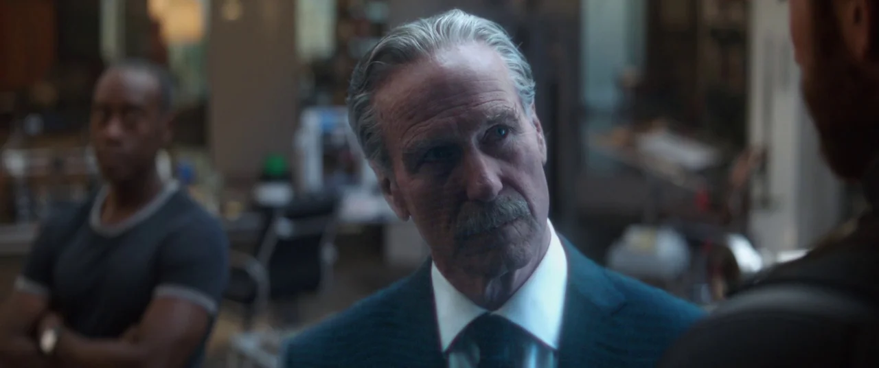 Avengers: Infinity War (2018) movie still: closeup — A dimly lit corporate space with blurred office equipment visible in the background. An older…