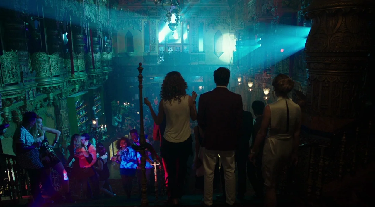Urge (2016) movie still: wide — A lavish multi-level nightclub features ornate gold railings and dramatic teal stage lighting. A group of people…
