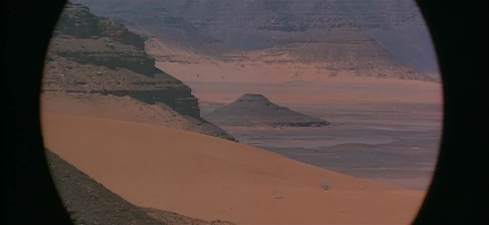 Lawrence Of Arabia movie still: establishing — A vast desert expanse features sand dunes and rocky plateaus under clear skies. The view is framed…