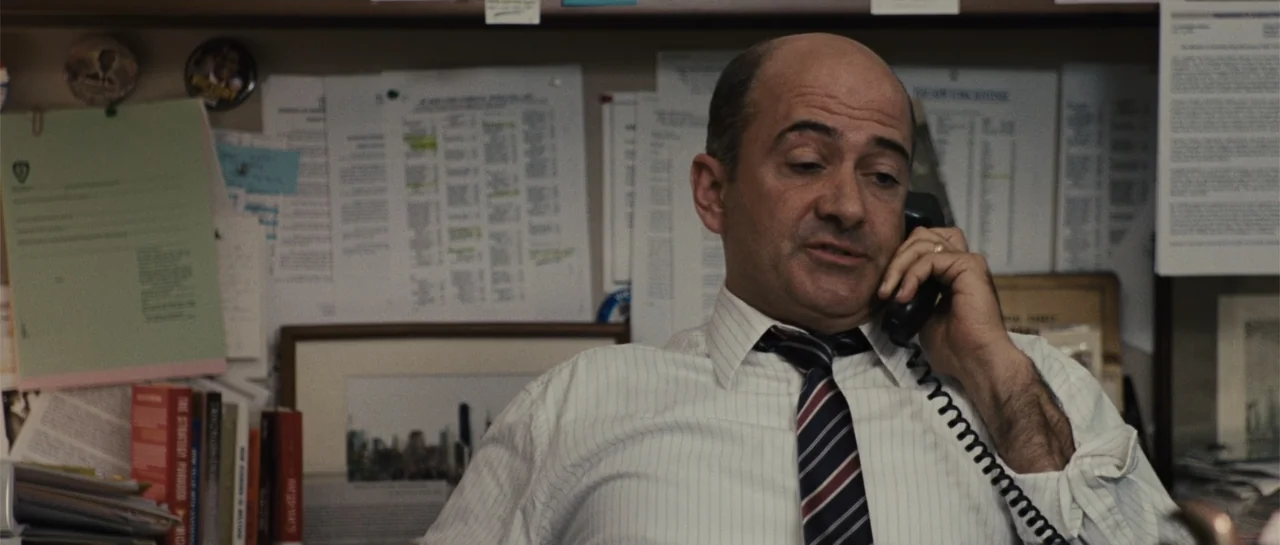 Going the Distance (2010) movie still: medium — A cluttered office wall covered in pinned documents and papers serves as the backdrop. A man in a…