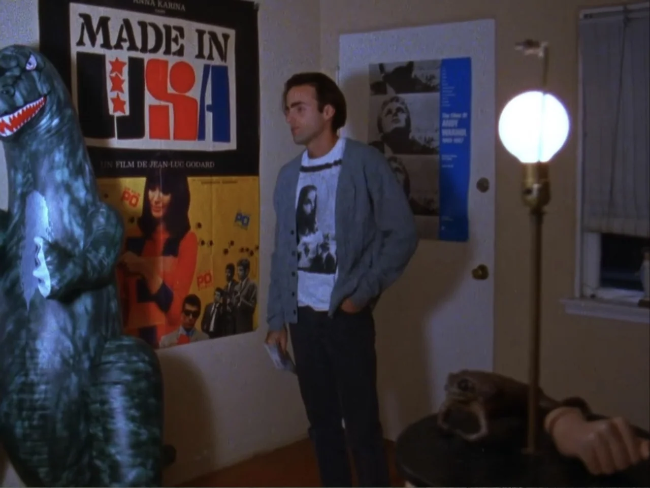 The Living End (1992) movie still: medium — A room with beige walls features several posters and a standing lamp.