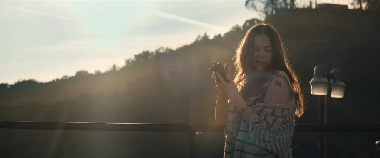 Equation of Love and Tone Deafness (2015) movie still: medium — A woman stands on an outdoor balcony during golden hour with a hazy hillside…