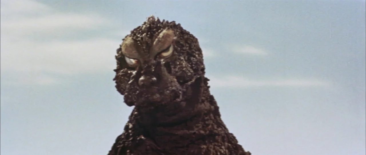 Mothra Vs Godzilla (1964) movie still: closeup — A close-up shot focuses on the head and neck of a reptilian monster. The creature faces the camera…