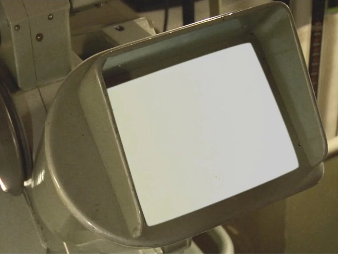 Don't Expect Too Much (2011) movie still: closeup — A close view of an old microfilm reader with a stark white glowing screen. The metallic frame of…