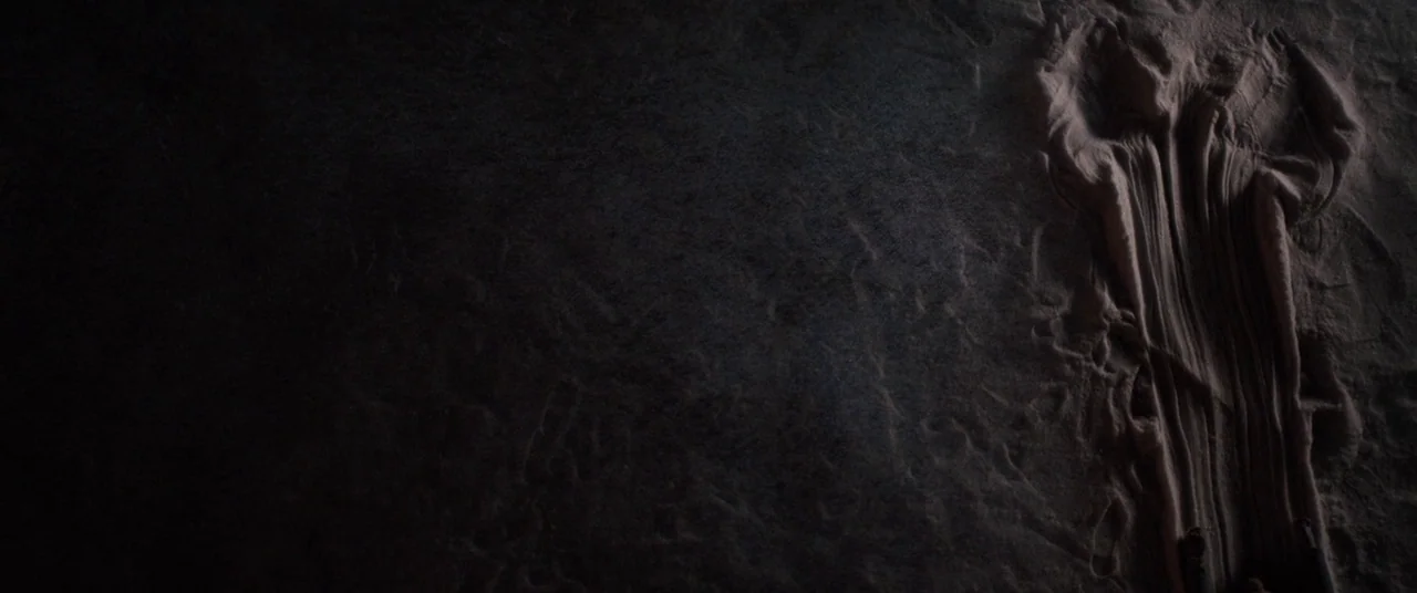 Black Christmas (2006) movie still: wide — A flat expanse of dark sand extends across the frame under low light. A human-shaped impression is…