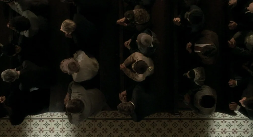 The Long Day Closes (1992) movie still: wide — A top-down view shows rows of wooden church pews filled with seated individuals. People are…