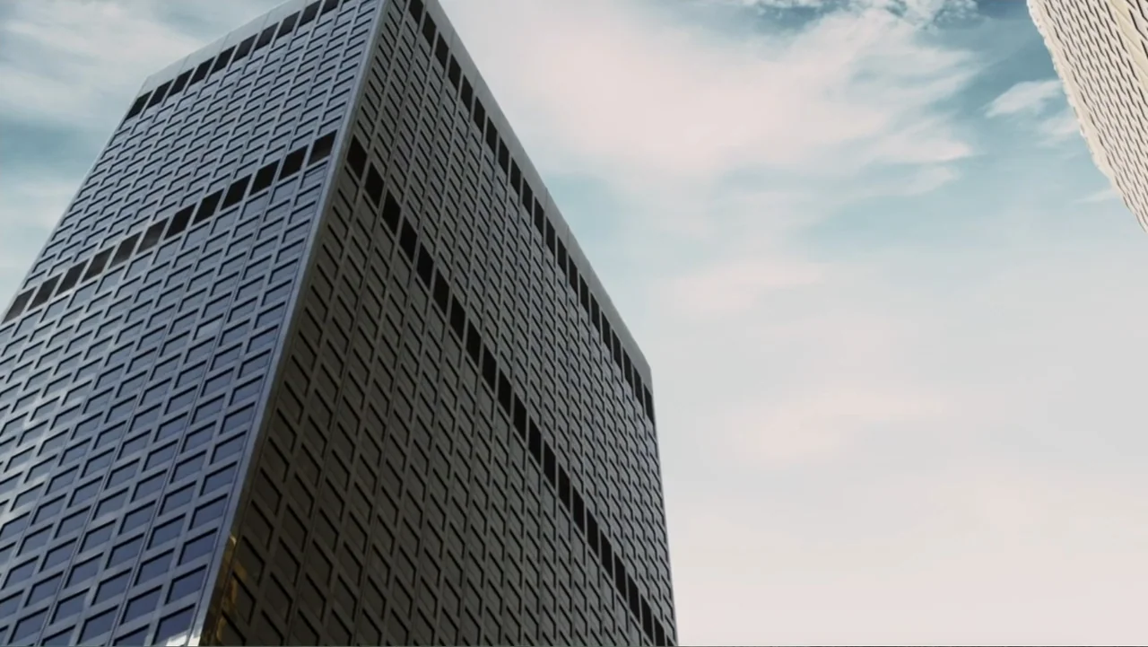 Alex & Emma (2003) movie still: establishing — A tall skyscraper dominates the frame with a repetitive grid of rectangular windows. The building…