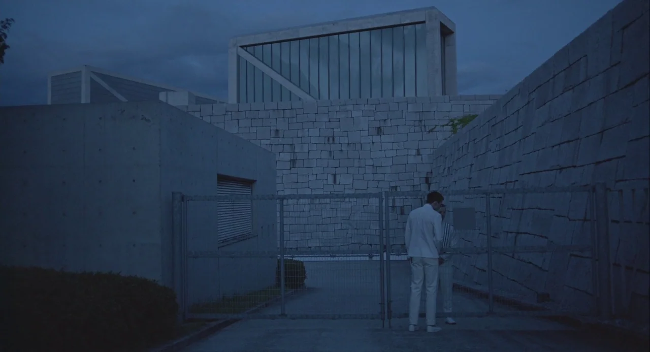 Equals (2015) movie still: wide — A modern architectural complex features concrete walls, stone block masonry, and tall glass panels. Two men in…