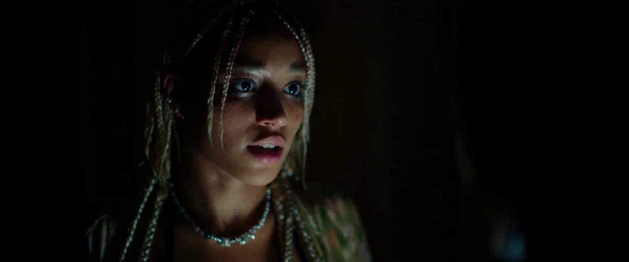 Bodies Bodies Bodies (2022) movie still: closeup — A close-up of a young woman's face illuminated within a dark, undefined interior space. She gazes…