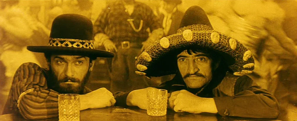 Lemonade Joe (1964) movie still: medium — Two men stand at a wooden counter in a crowded saloon setting. They both lean their arms forward on the…