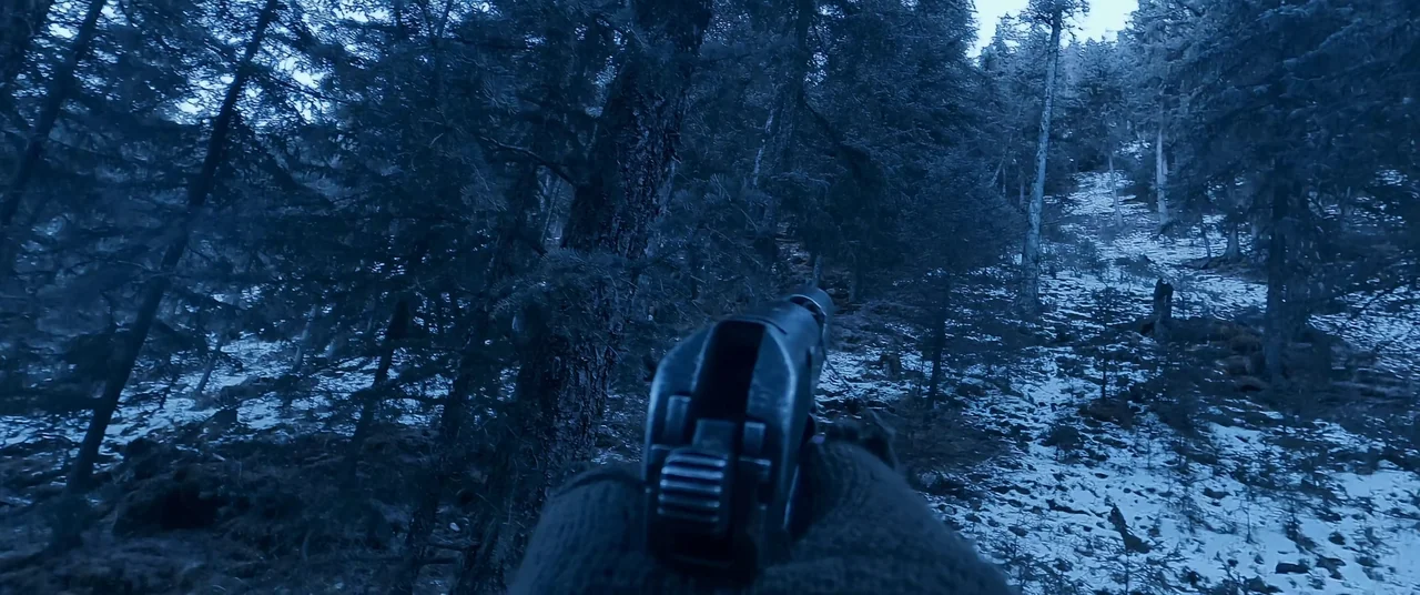 One And Four (2021) movie still: closeup — A snowy, wooded hillside sits under a deep blue twilight sky. A hand wearing a tactical glove holds a…